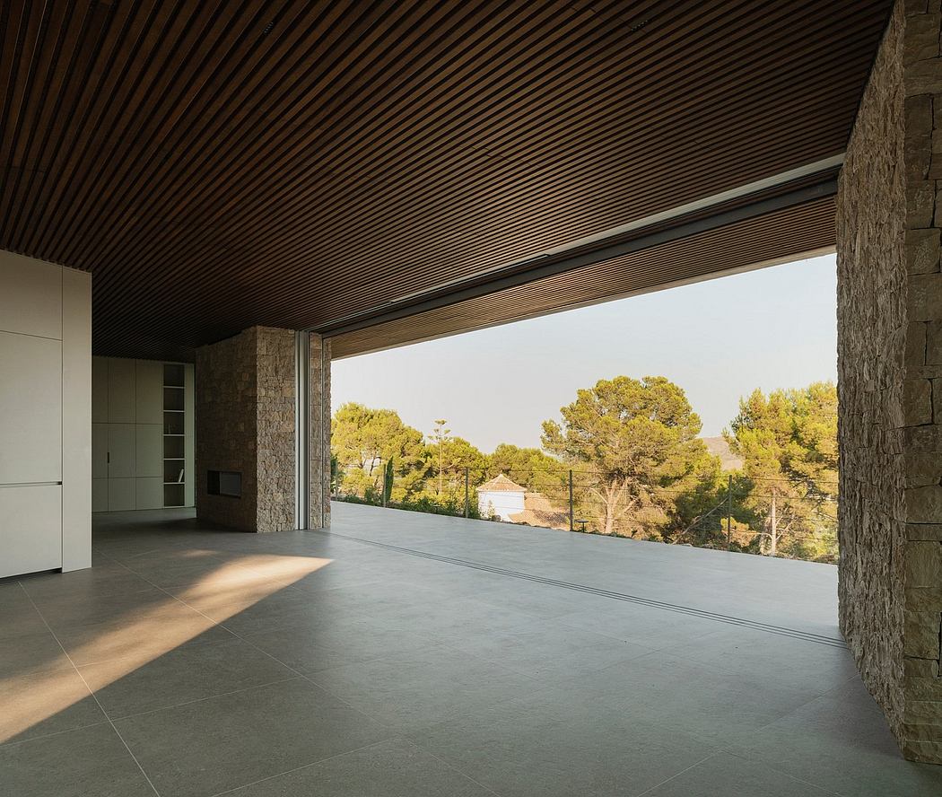 A modern interior with a wooden ceiling, stone walls, and a large glass window overlooking a picturesque landscape.