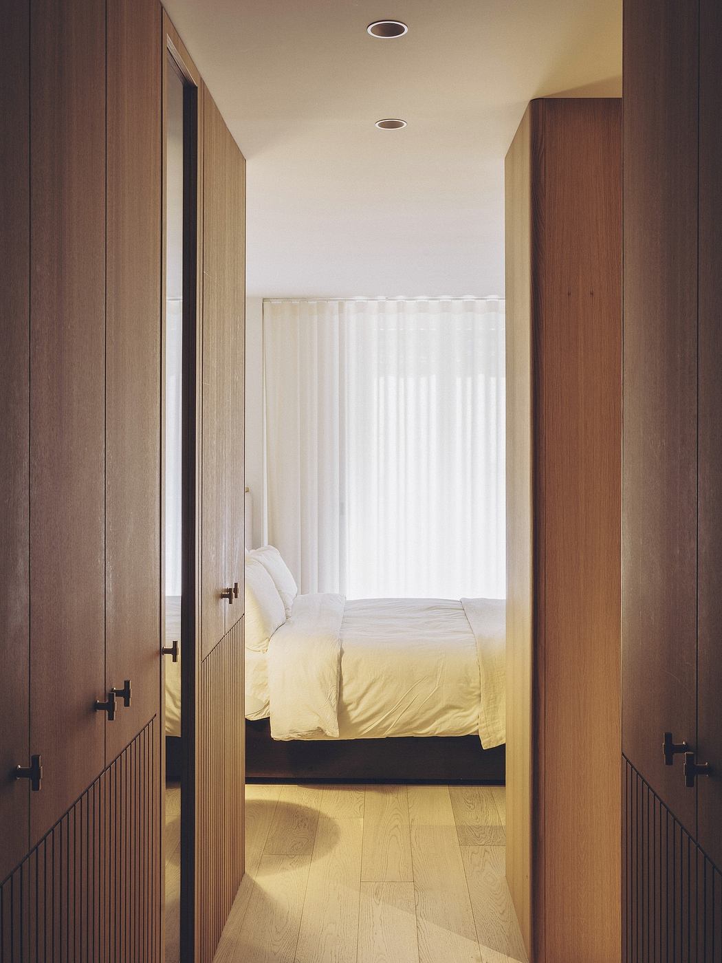 Warm-toned, minimalist bedroom with recessed lighting and wooden built-in cabinetry.