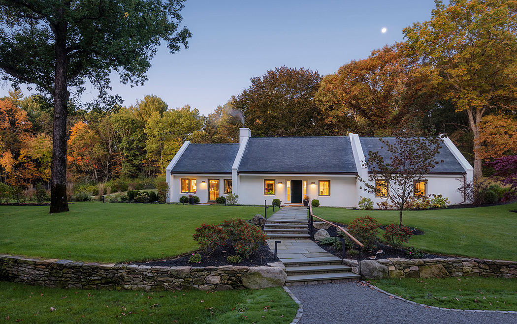 Stately white home with gray roof, surrounded by lush autumn foliage and stone pathway.