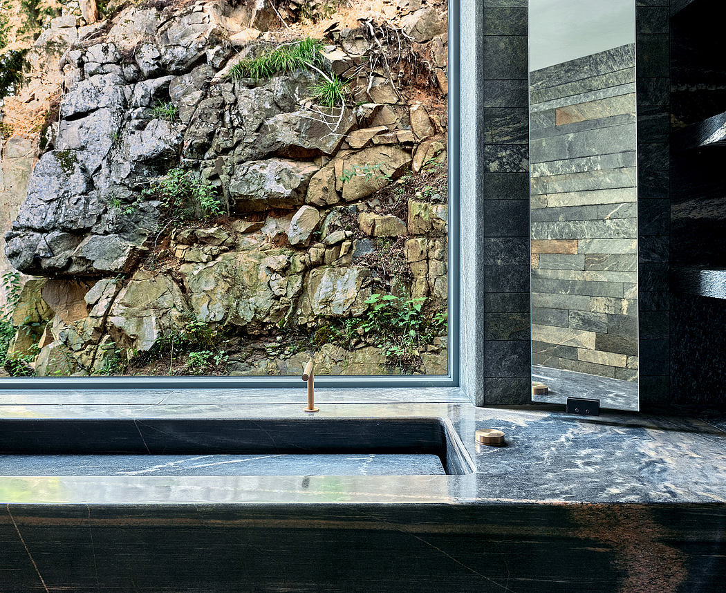 A contemporary bathroom with a stone wall backdrop, minimalist slate fixtures, and a deep soaking tub.