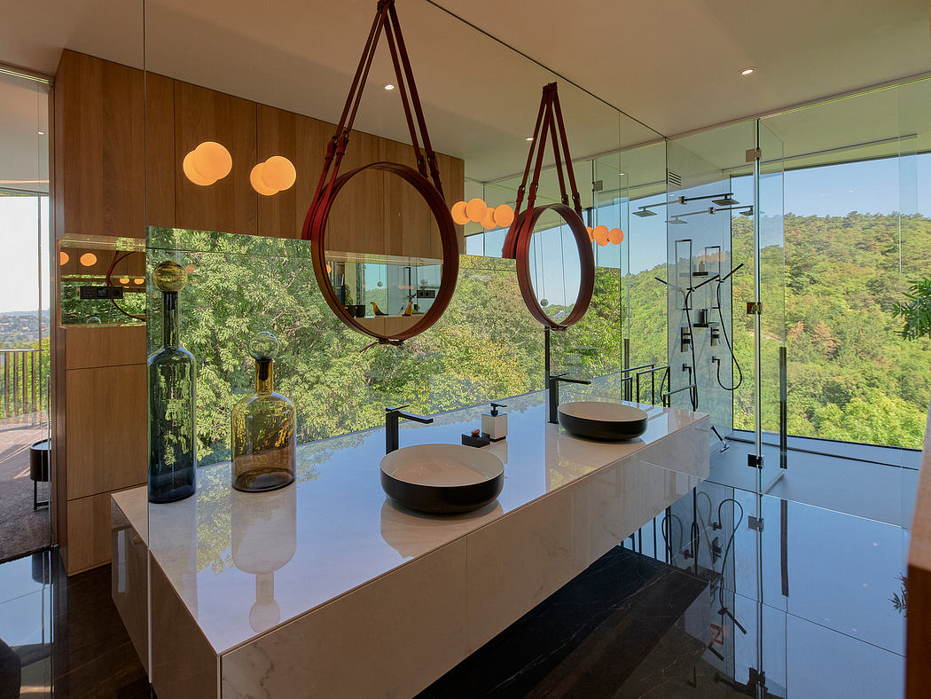 A modern, minimalist bathroom with circular mirrors, pendant lights, and a stunning forest view.