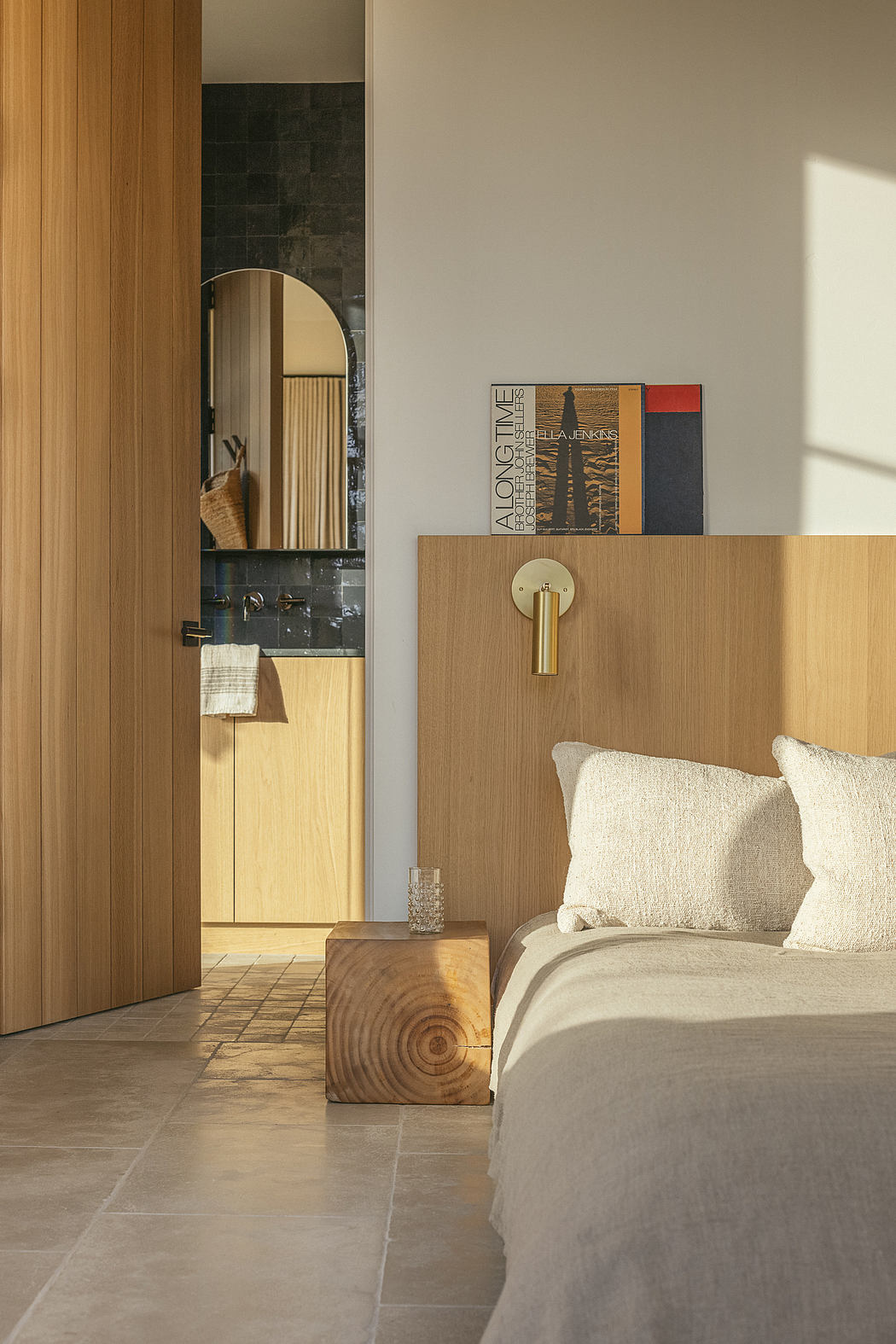 The room features a minimalist design with wooden panels, a stone floor, and a brass lamp.