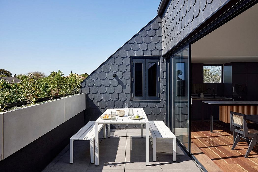 A modern exterior with dark slate tiles, a deck, and a minimalist dining set.