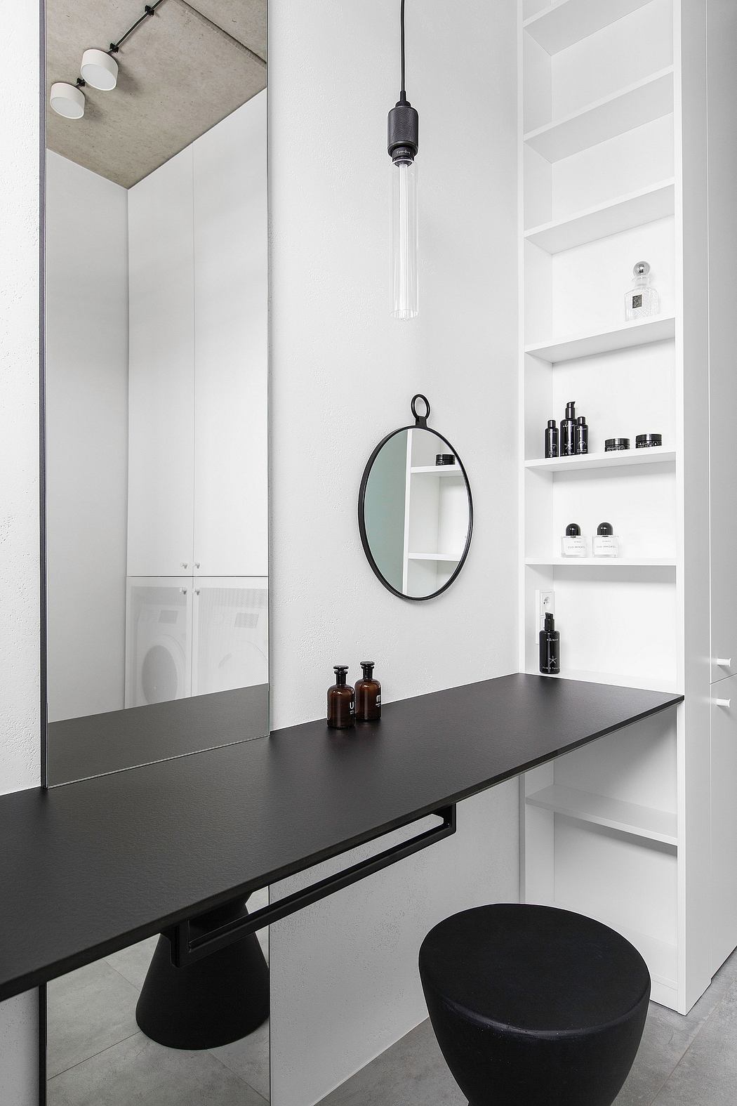 Minimalist bathroom design with black vanity, oval mirror, and shelving for toiletries.