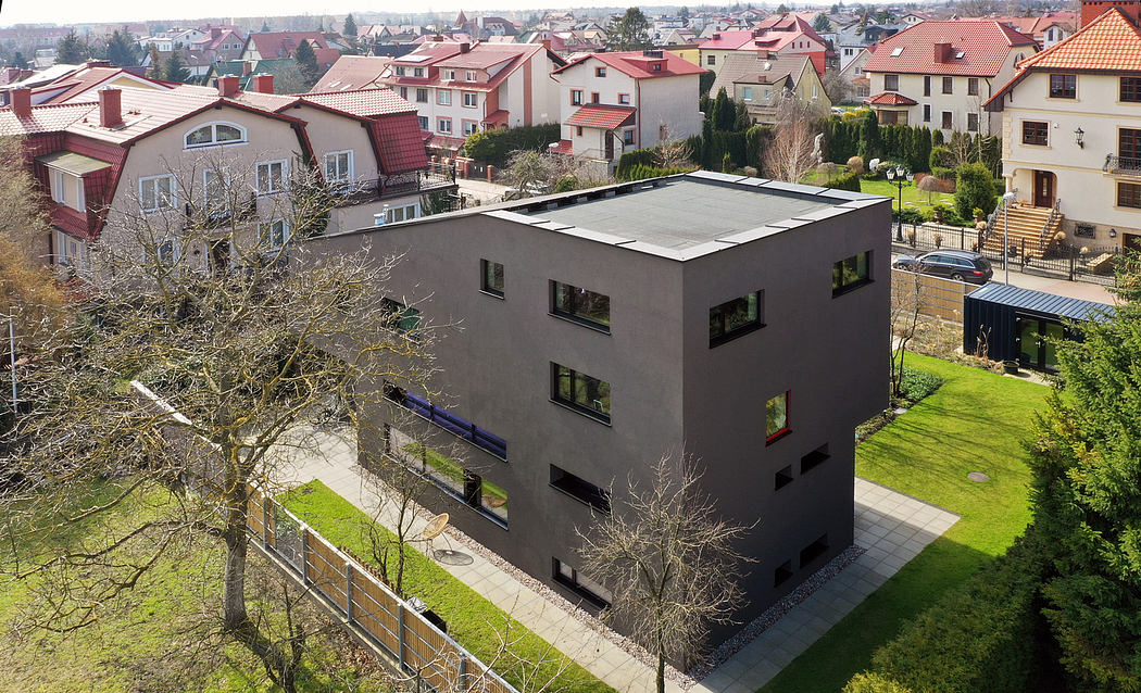 Modern, multi-story residential building with flat roof, large windows, and lush surrounding greenery.