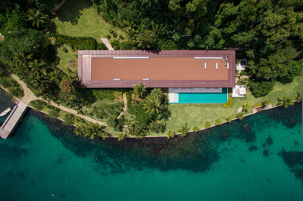 An aerial view of a sleek, modern villa with a rectangular structure and a pool overlooking lush greenery.
