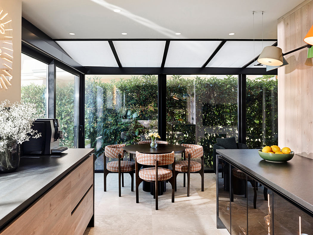 Modern kitchen-dining area with sleek black steel frame, natural wood cabinetry, and lush greenery views.