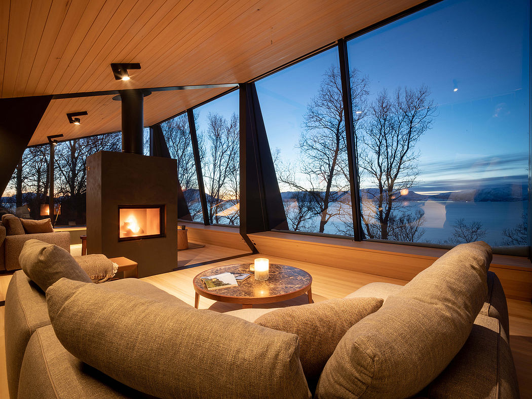 Cozy living room with a fireplace, wooden ceiling, and large windows overlooking a lake.
