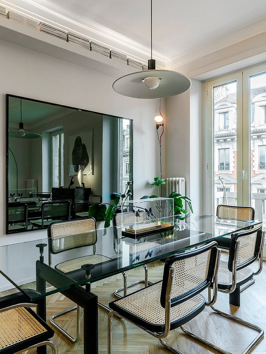Modern apartment interior with glass table, cane chairs, and a large pendant light fixture.