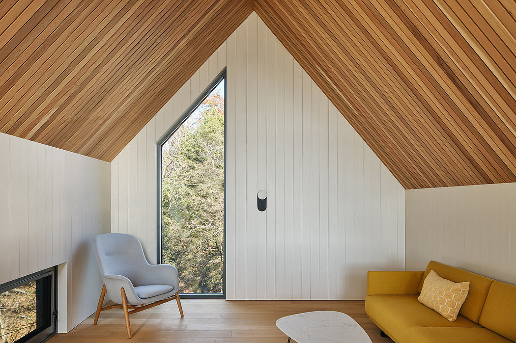 A modern, cozy cabin interior with a cathedral ceiling, wooden paneling, and a large window overlooking the forest.