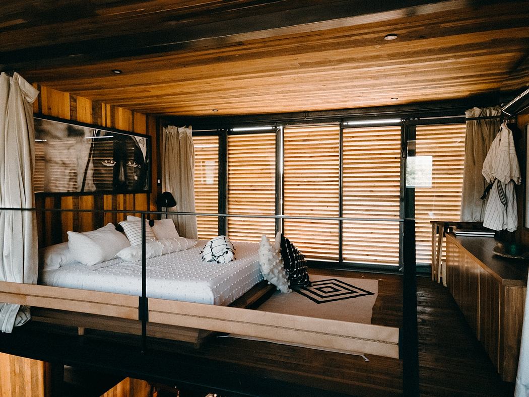 A cozy wooden bedroom with floor-to-ceiling curtained windows, a plush bed, and a statement artwork.