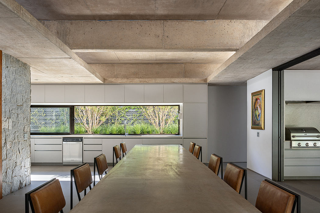 Minimalist kitchen with concrete walls, large windows, and a long wooden dining table.