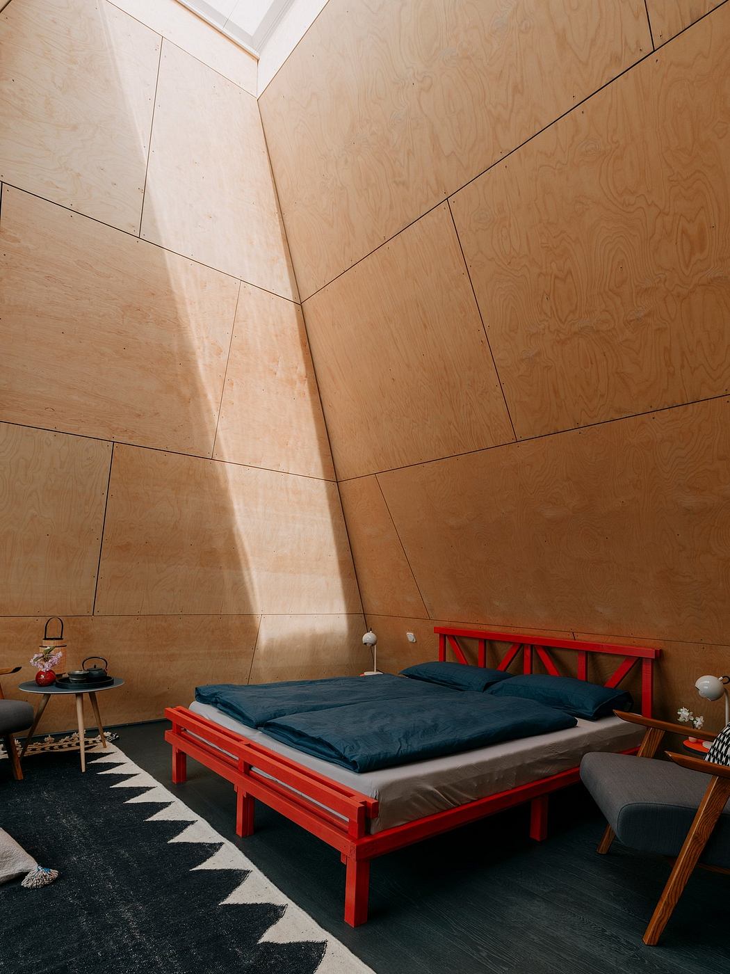 Minimalist wooden interior with geometric patterns, red bed frame, and natural lighting.