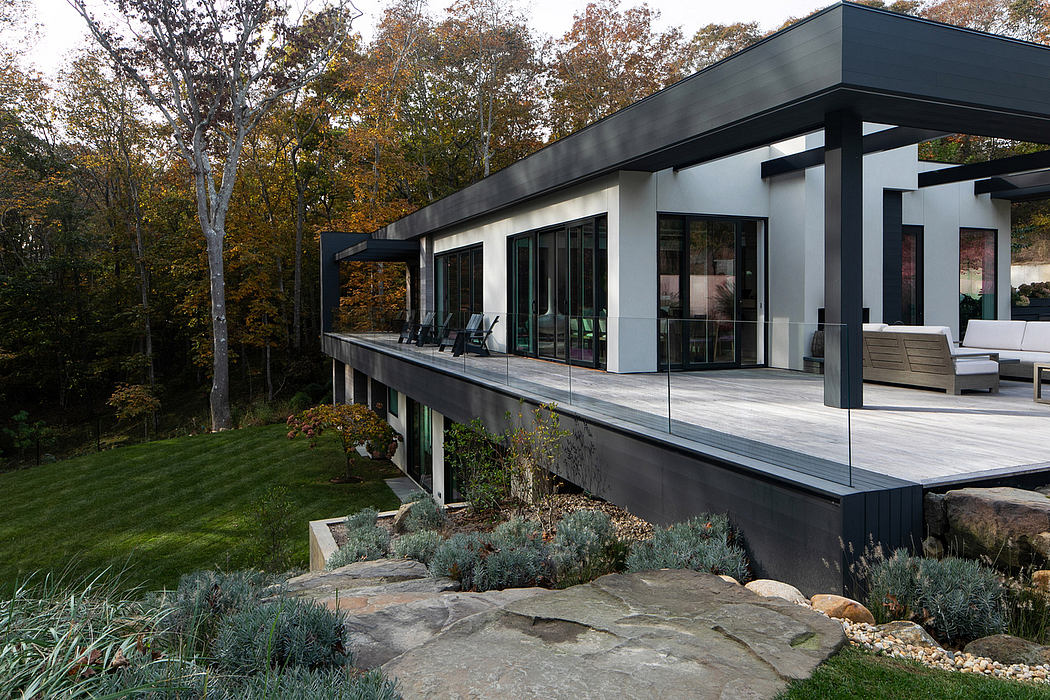 A modern glass-enclosed house elevated on a rocky hillside surrounded by lush foliage.