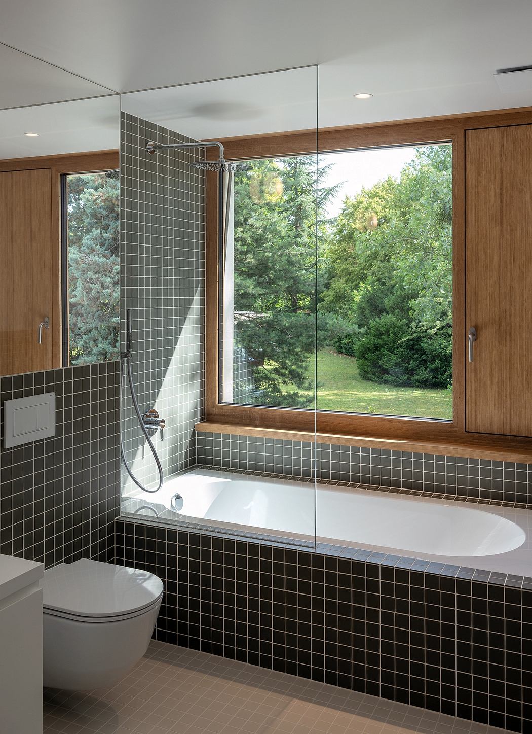 A modern, open bathroom with a large window overlooking a lush, wooded landscape.