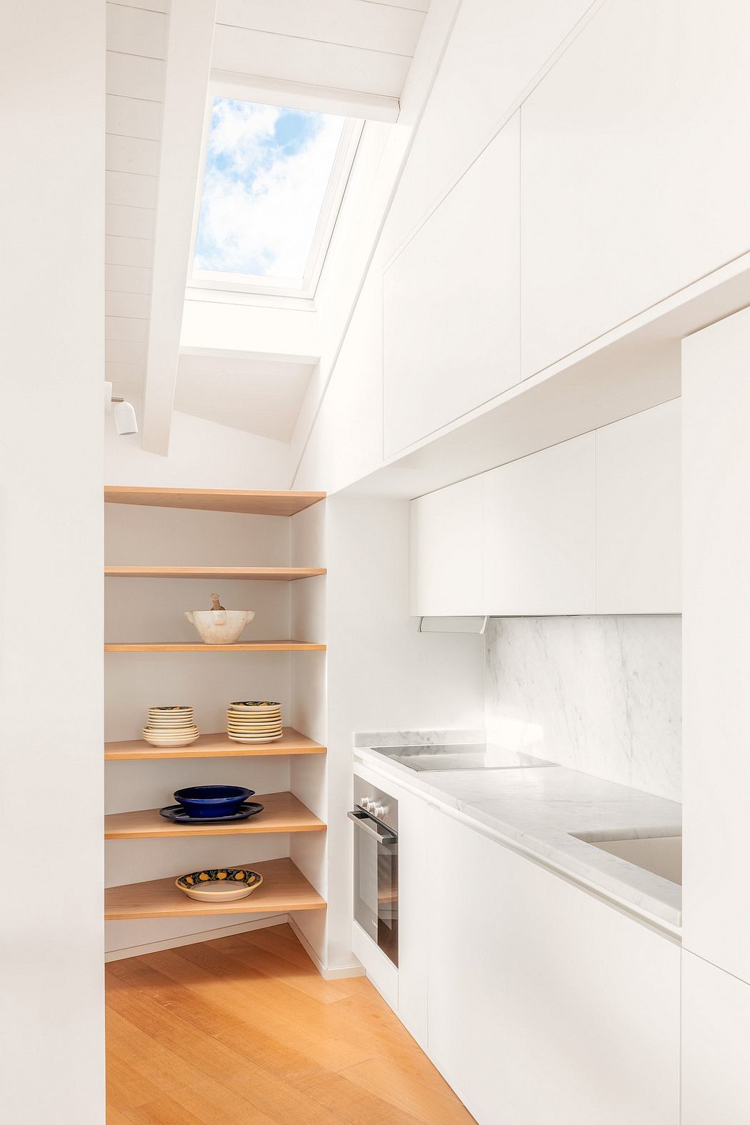 Bright, airy kitchen with built-in shelving, large window, and sleek marble countertops.