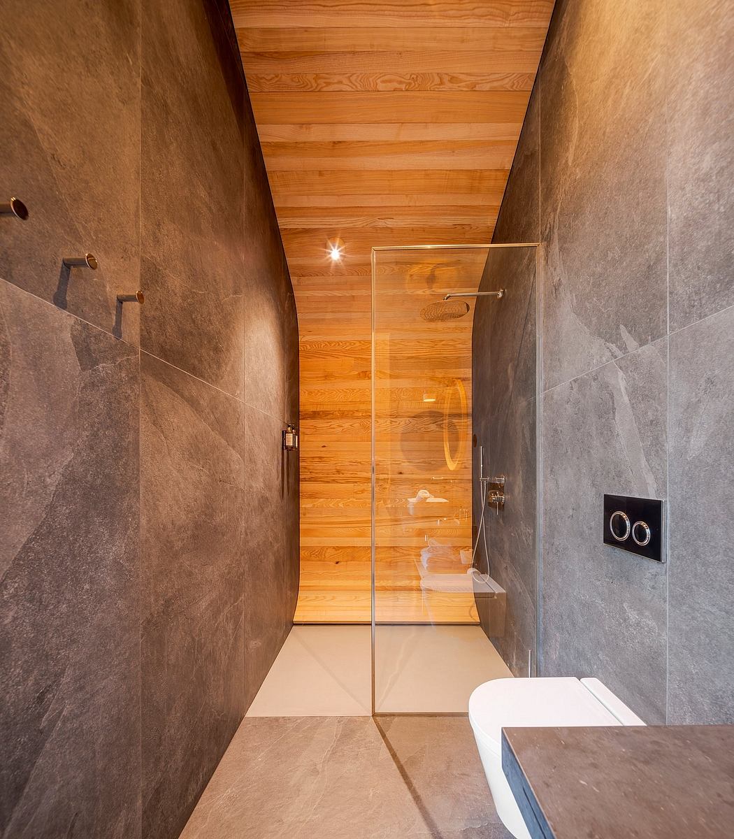 A modern bathroom with a wooden panel ceiling, glass shower enclosure, and gray tile walls.