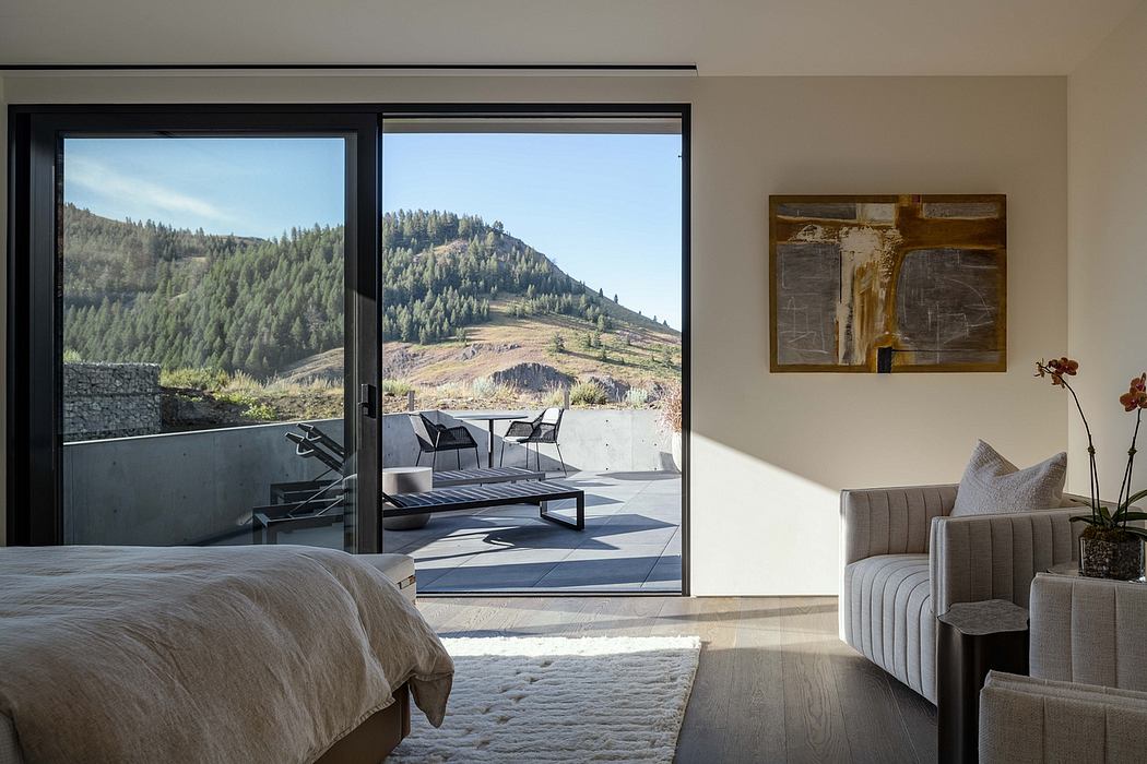 Minimalist bedroom with floor-to-ceiling windows offering scenic mountain views and a cozy seating area.