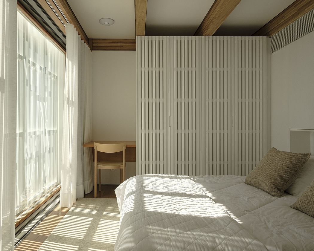 A cozy bedroom with wooden beams, textured wall panels, and a large window letting in natural light.