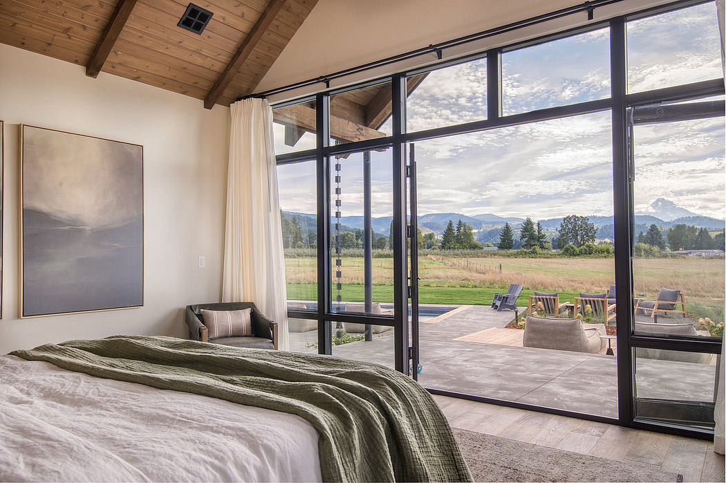 Cozy bedroom with rustic wooden ceiling, floor-to-ceiling windows overlooking scenic mountainscape.