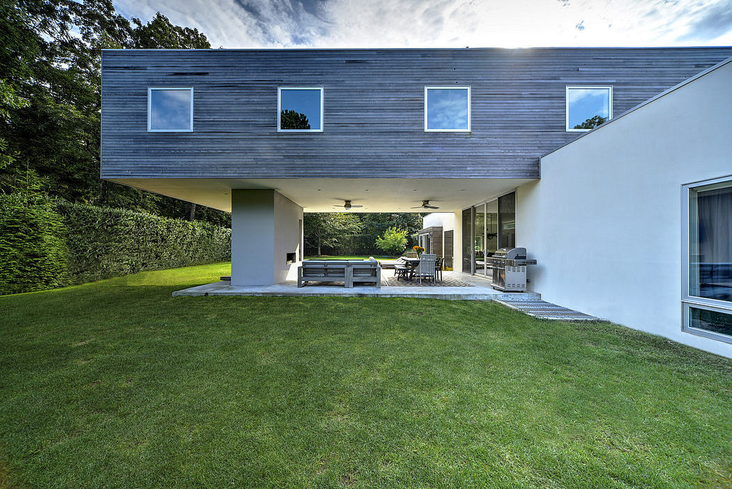 Modern, two-story residence with clean lines, large windows, and a covered outdoor living space overlooking a lush, well-manicured lawn.