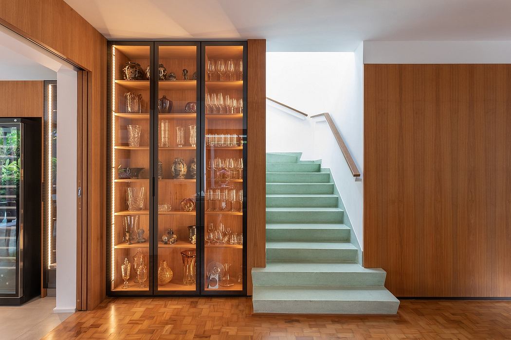 Well-designed wooden shelves display an elegant collection of glassware and decor, complementing the sleek concrete staircase.