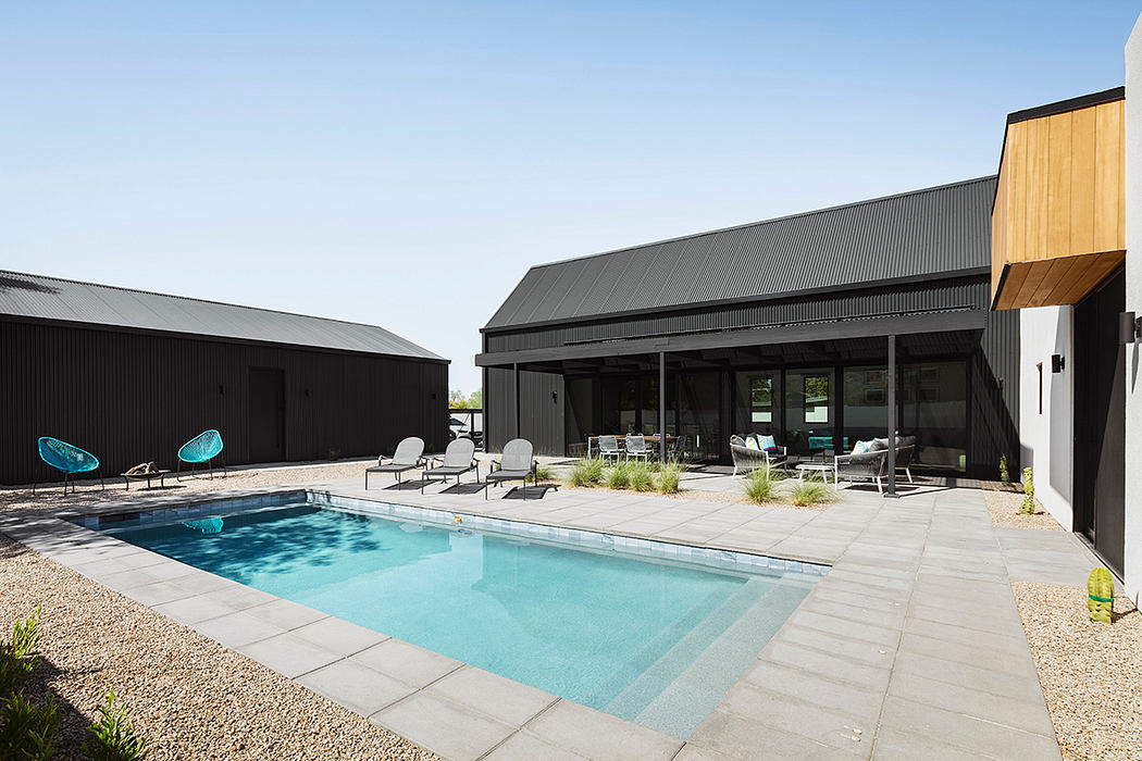 The image shows a modern, sleek house with a black exterior, large windows, and a swimming pool surrounded by lounging chairs.