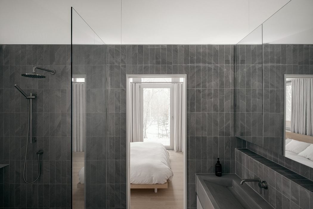 Minimalistic, grey-tiled bathroom with transparent glass shower and view to bedroom.