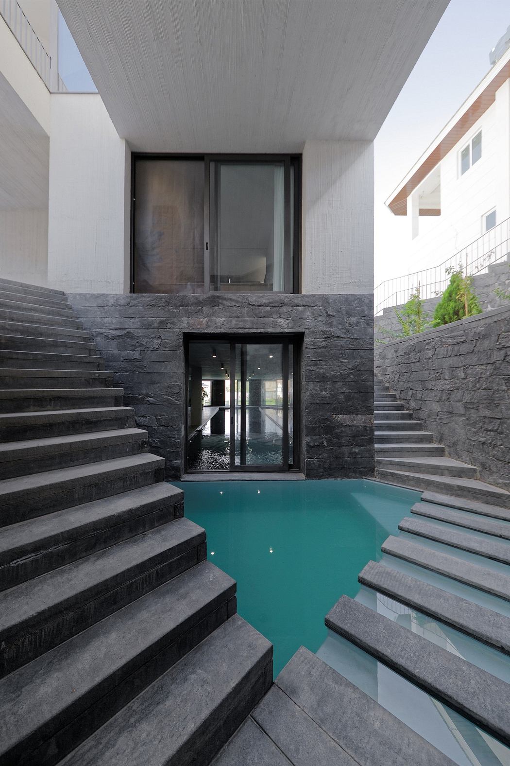 Sleek modern architecture with striking black stone steps leading to a tranquil pool.
