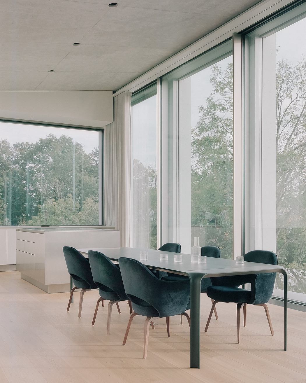 Large glass windows frame a minimalist dining area with sleek black chairs and a modern table.