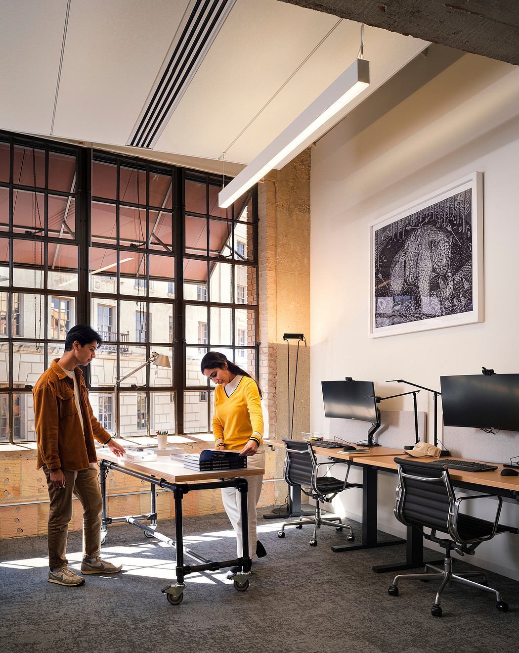 Bright, industrial-style office with large windows, modern furniture, and artwork on the walls.