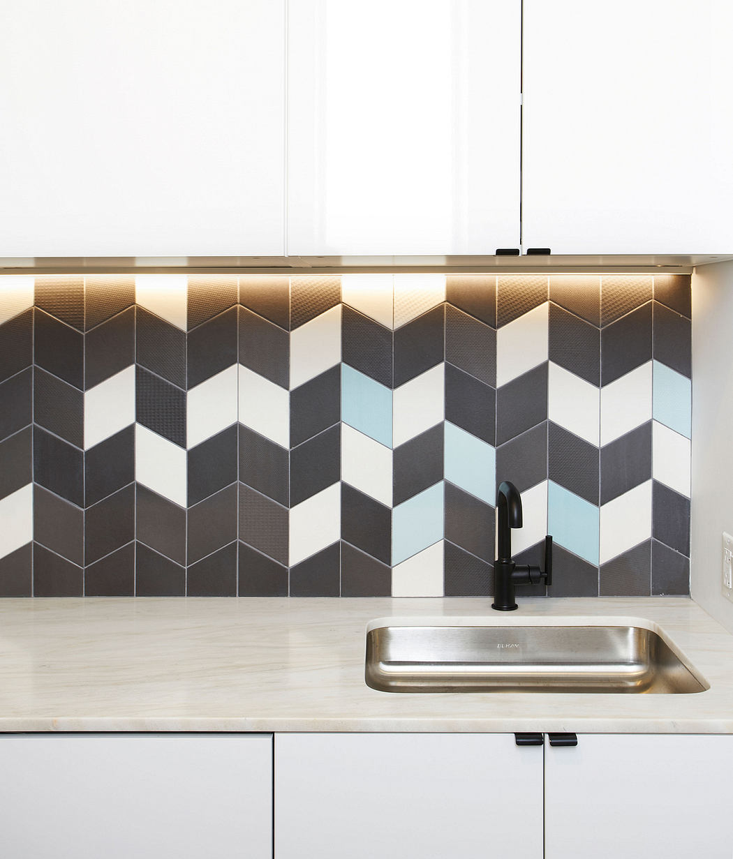 A modern kitchen backsplash featuring a geometric tile pattern in shades of gray and blue, complementing the stainless steel sink.