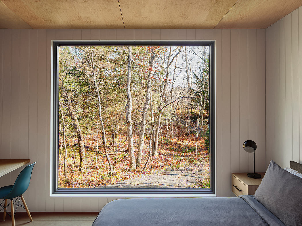 A spacious bedroom with large window overlooking a lush wooded landscape.
