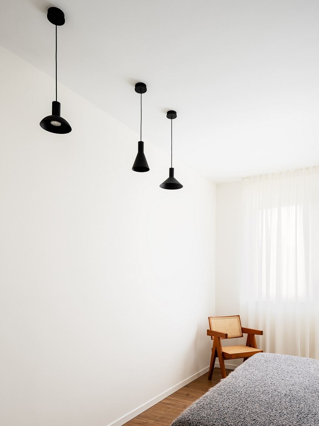 Minimalist room with black pendant lights and a wooden armchair on a gray rug.