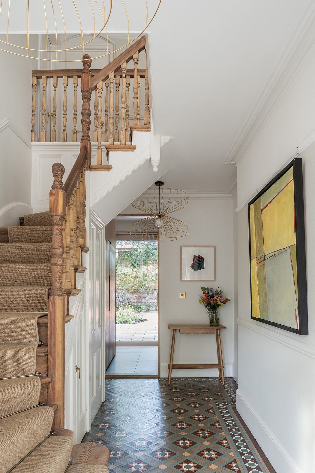 Inviting entryway with ornate wood staircase, patterned tile floor, and stylish lighting.