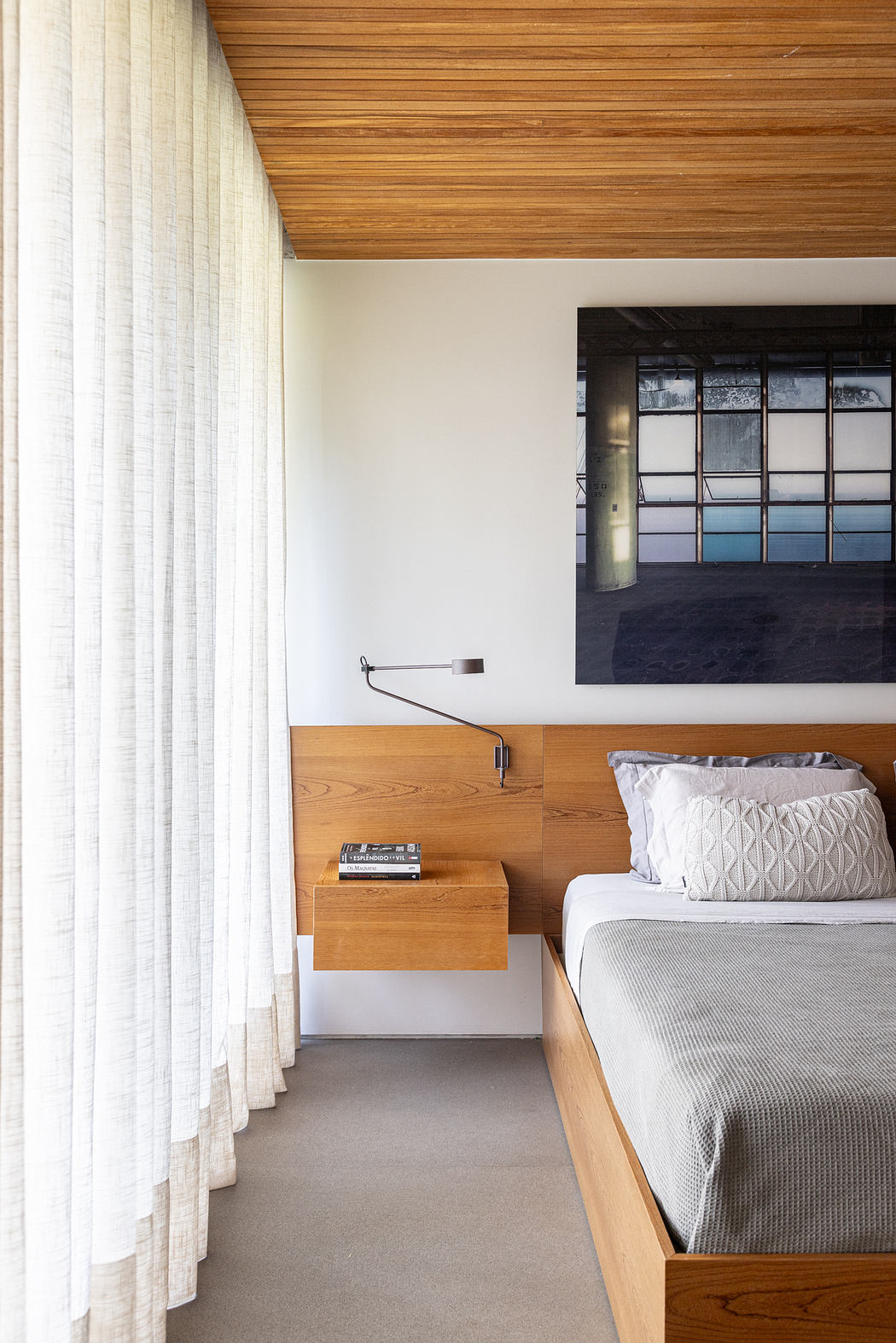 Minimalist bedroom with wood paneled ceiling, curtains, and built-in bedside table.