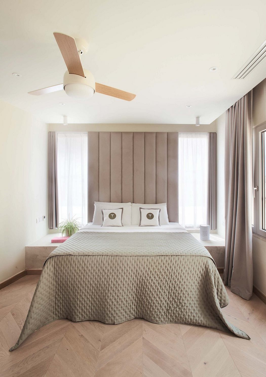 Minimalist bedroom with wood ceiling fan, plush bedding, and vertical upholstered wall.