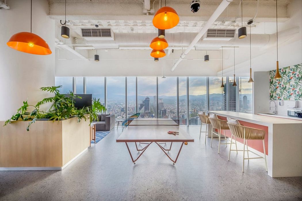 Bright, modern office space with floor-to-ceiling windows, tropical plants, and colorful lighting fixtures.