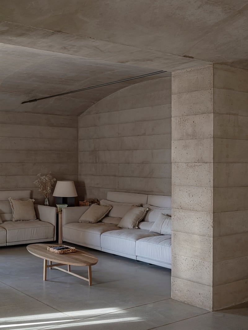 A minimalist living room with concrete walls, soft furnishings, and a wooden coffee table.
