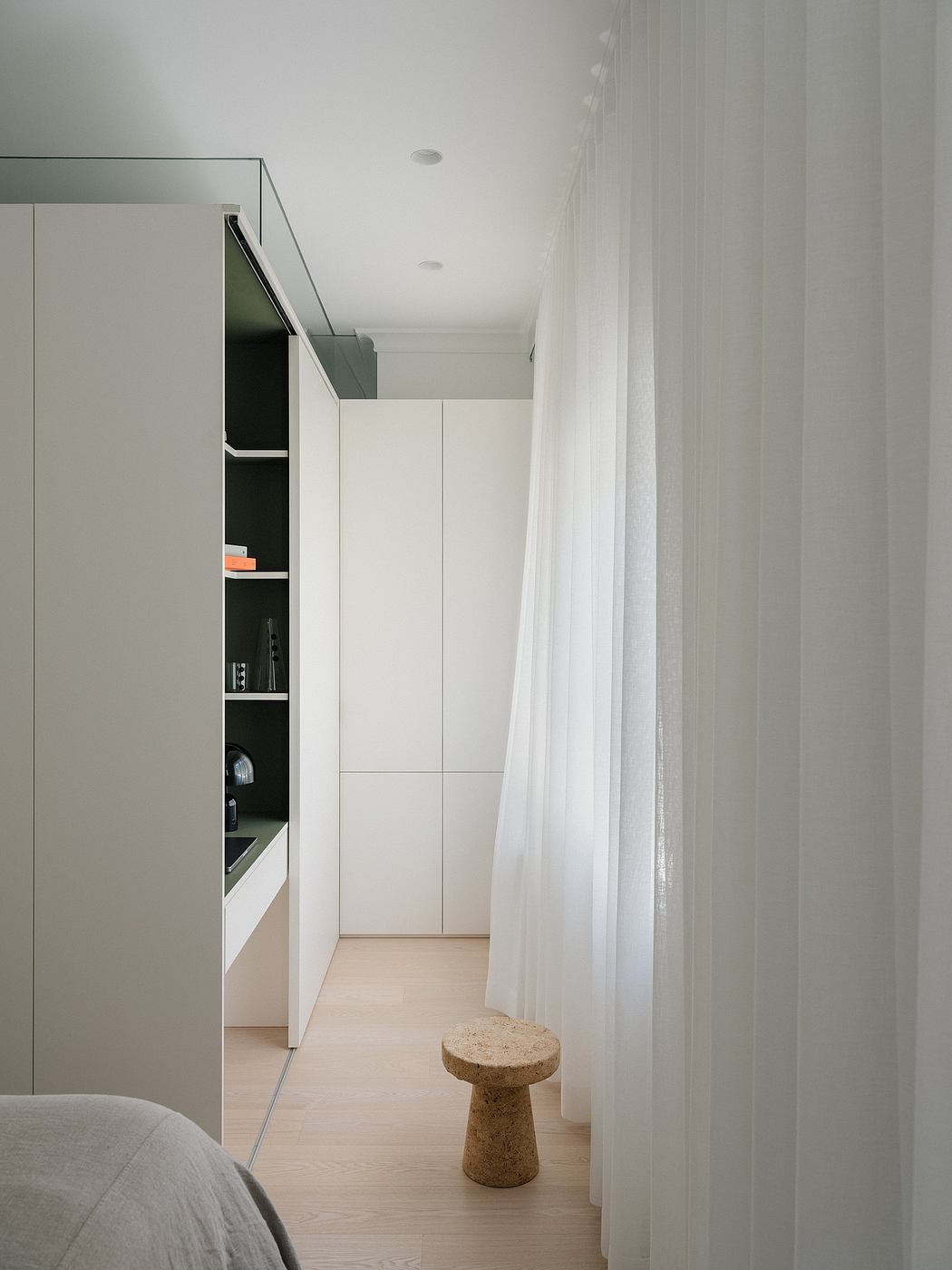 Minimalist bedroom interior with built-in storage units and a cork stool.
