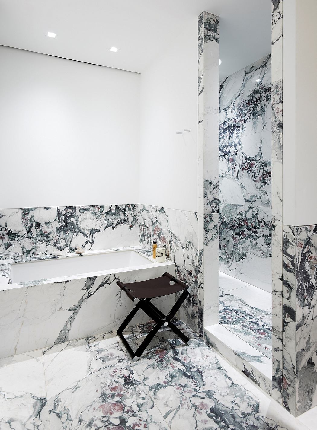 Sleek, modern bathroom features striking marble walls, minimalist vanity, and a folding stool.