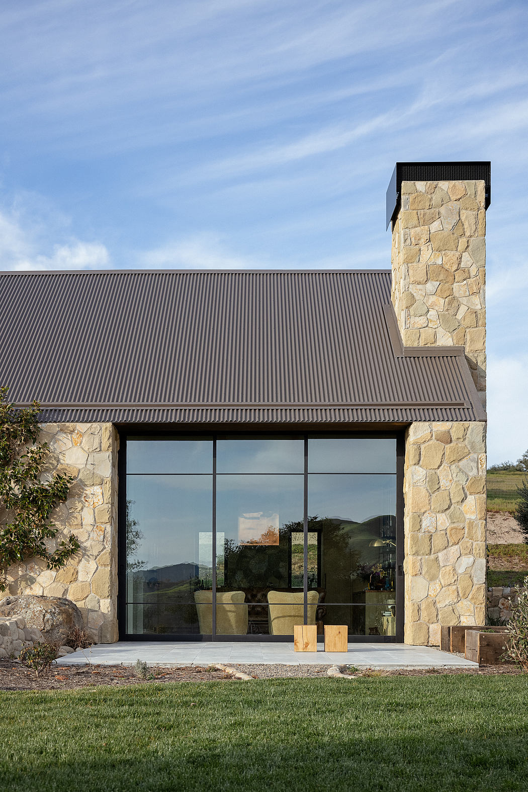 Modern stone and metal facade with large glass windows overlooking lush outdoor space.
