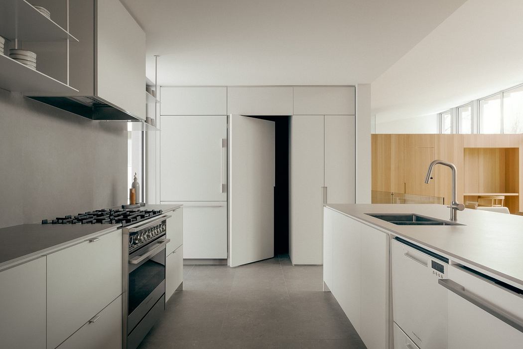 A modern, minimalist kitchen with sleek white cabinetry, stainless steel appliances, and concrete floors.