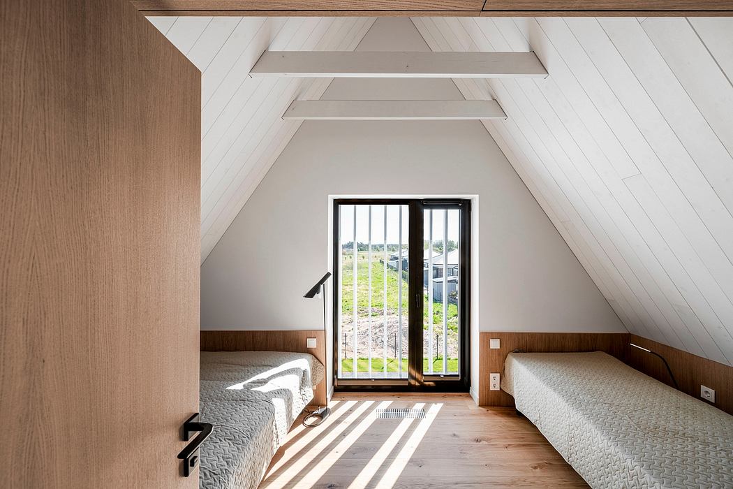 Warm, modern attic bedroom with wood-paneled walls and slanted ceiling. Tall windows offer scenic countryside view.