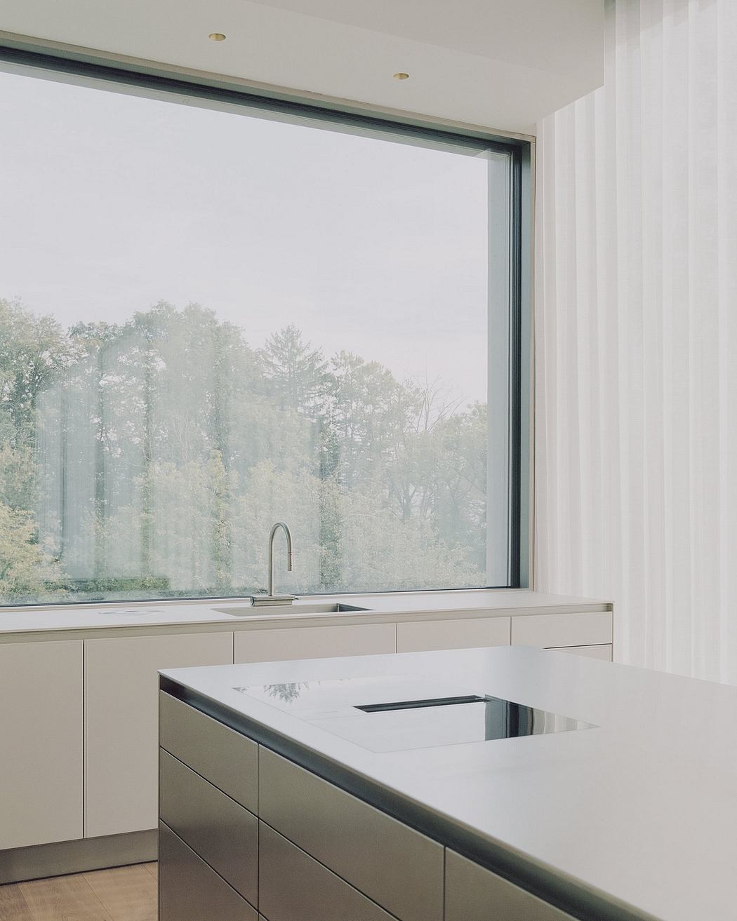 A modern kitchen with a large window offering a serene forest view, featuring clean lines and minimalist design.