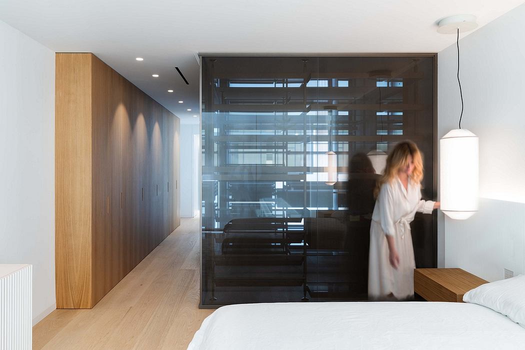 Minimal modern bedroom with glass divider, wooden cabinetry, and natural lighting.