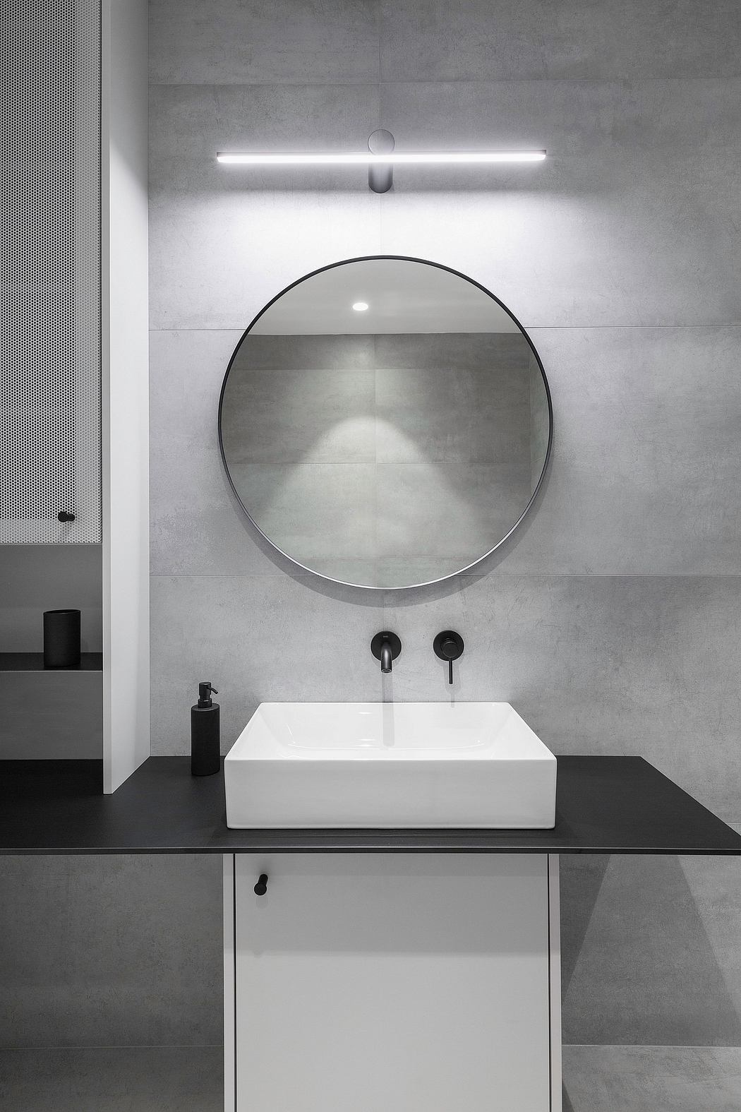 A minimalist bathroom design featuring a large circular mirror, a white sink, and concrete walls.