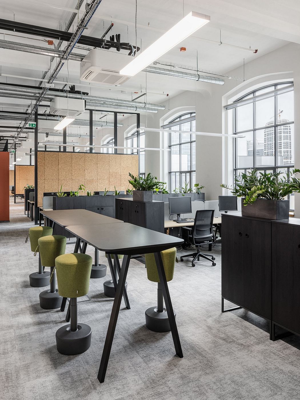 Open-concept office space with modern, industrial design featuring large windows, exposed ceiling, and minimalist furniture.