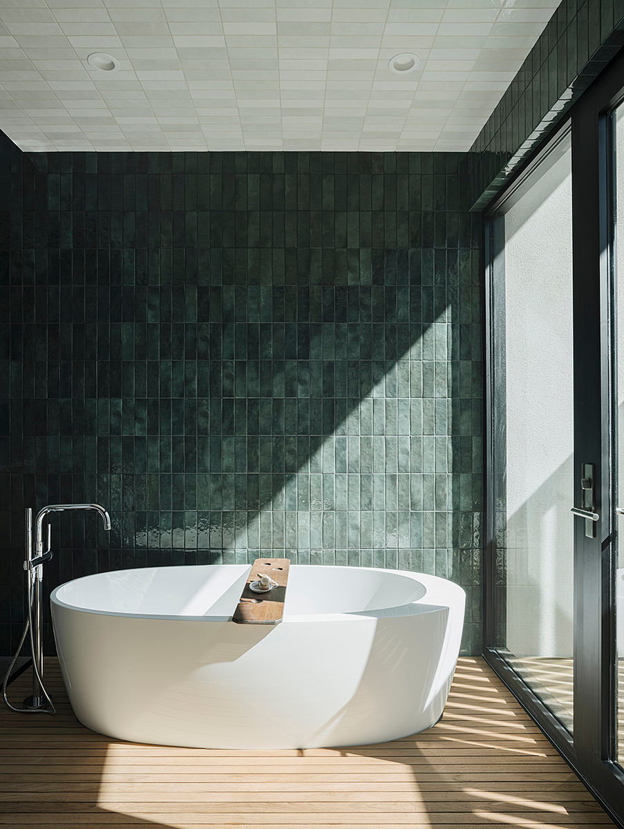 Luxurious bathroom with freestanding tub, dark tiled walls, and wooden flooring.