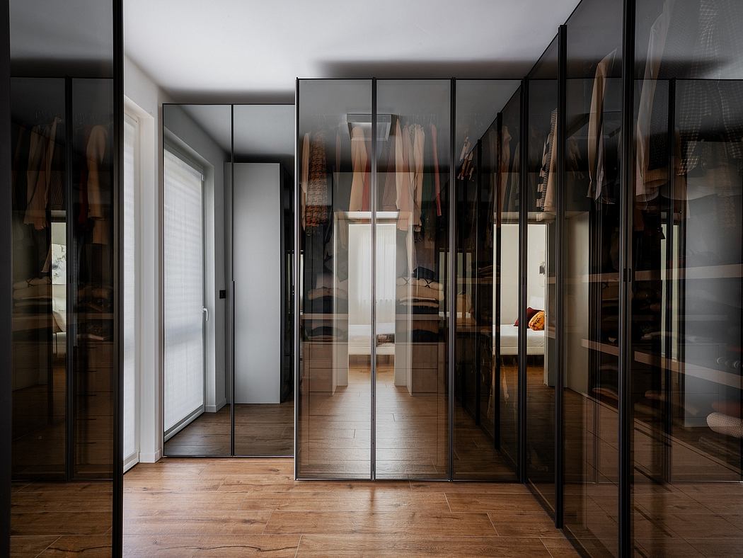 Modern, glass-enclosed walk-in closet with dark wood flooring and minimalist design.